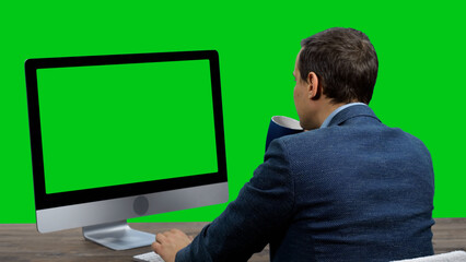 Young adult businessman working on computer with green screen and drinking tea or coffee against green background