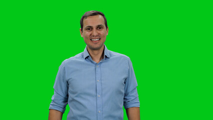 Fototapeta premium Portrait of young smiling man in light blue colored shirt standing against green background
