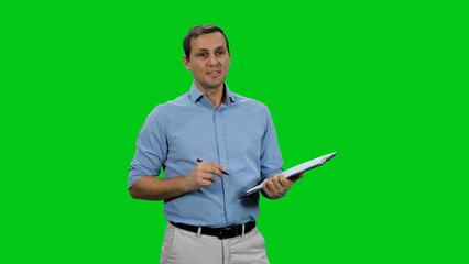 Handsome young businessman wearing light-blue shirt taking notes on clipboard against green background