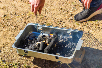 Portable grill with burning charcoal and smoke by riverbank.
