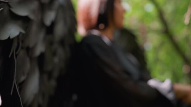 Close up of archer black wings of in forest, soft sunlight highlighting texture before release of arrow, background blurred with calm green tones, atmosphere filled with focus