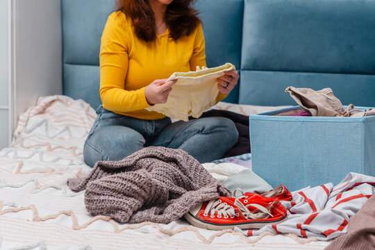 A young woman sorting clothes and packing into cardboard boxes. Donations for charity, help low income families, declutter home, sell online, moving moving into new home or recycling - Powered by Adobe