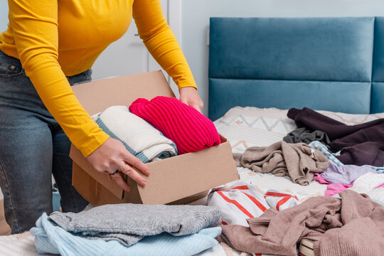A young woman sorting clothes and packing into cardboard boxes. Donations for charity, help low income families, declutter home, sell online, moving moving into new home or recycling