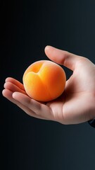 Hand holding an apricot, focusing on its smooth texture and warm orange color.
