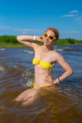 Portrait of a beautiful young sexy caucasian woman with wet red hair on the beach in a yellow bikini and yellow sunglasses. Kallaste beach, Lake Peipus, Estonia. 