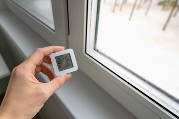Fototapeta premium High indoor humidity indicated by a digital hygrometer showing 80 percent, next to a wet window with visible condensation in winter, indoor climate control concept.