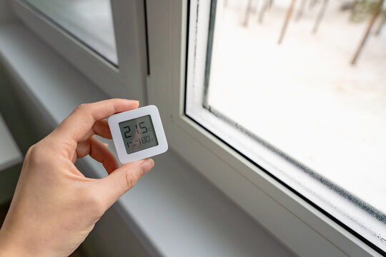 High indoor humidity indicated by a digital hygrometer showing 80 percent, next to a wet window with visible condensation in winter, indoor climate control concept.