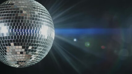 Shiny silver disco ball with mirror tiles reflecting light and lens flares against a dark background creating a festive atmosphere