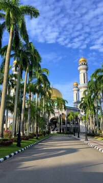 The golden dome and building of the Jamil Asra Hassan Al-Bolkiah Mosque in Bandar Seri Bagawan, Brunei Darussalam, are framed by tropical palm trees on a sunny day. Asia. 4К