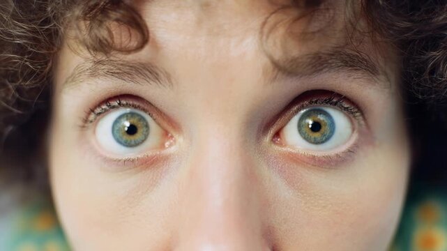 Surprised woman with bright blue green eyes stares into camera in humorous closeup creating playful comedy moment and expressive portrait concept