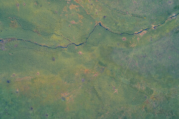 Abstract drone shot of a green grassy field with a small winding river flowing through it. The texture of the vegetation and the dark water channel create a scenic background for nature concepts.