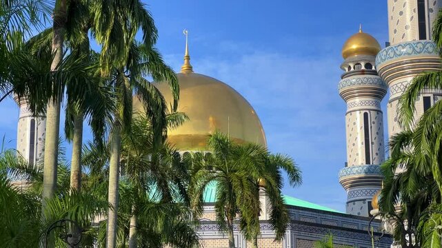 The golden dome and building of the Jamil Asra Hassan Al-Bolkiah Mosque in Bandar Seri Bagawan, Brunei Darussalam, are framed by tropical palm trees on a sunny day. Asia. 4К