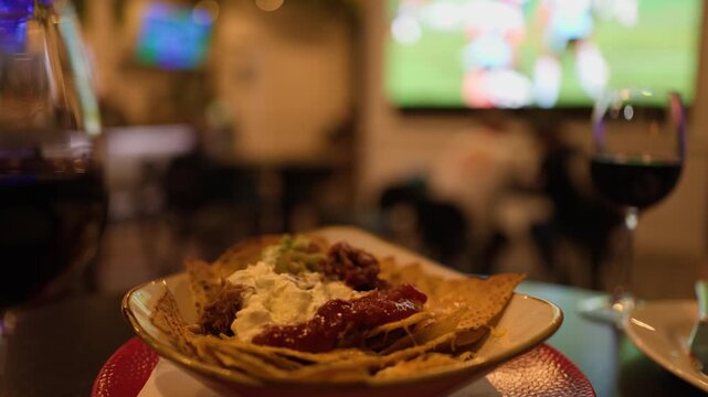 Hand Grabbing Nachos in Sports Bar with Wine and TV