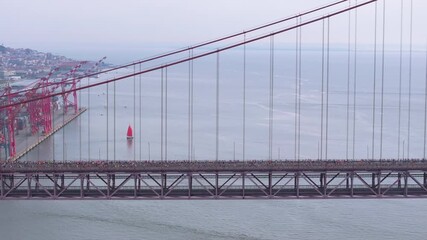 Side-on aerial drone shot of half marathon and 10K long-distance running event in Lisbon, Portugal, Europe. Runners crossing the iconic red 25th April bridge