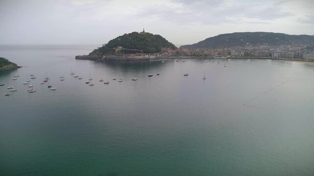 Aerial drone shot pulling back over La Concha Bay, flying above Miramar Palace with Monte Urgull and Castillo de la Mota and the San Sebasti&aacute;n waterfront in the background.