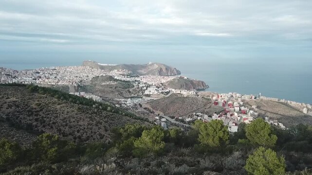 Stunning aerial drone footage flying over Al Hoceima. A panoramic view of the city buildings nestled along the blue Mediterranean coastline of Morocco.