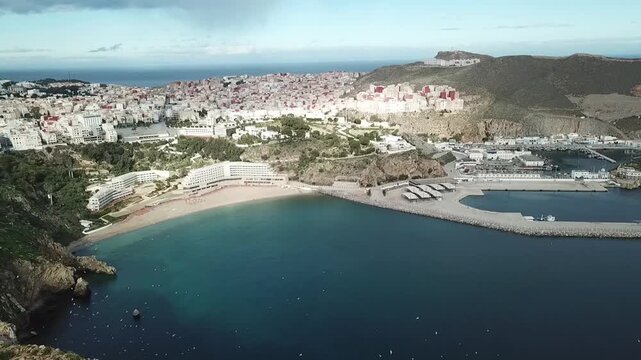Stunning aerial drone shot showing a golden sandy beach embraced by the rugged terrain of the Rif Mountains in Al Hoceima, Morocco.