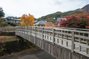 Wooden pedestrian bridge over river in autumn mountain village scenery near Saiko Lake, Saiko, Fujikawaguchiko, Minamitsuru District, Yamanashi, Japan