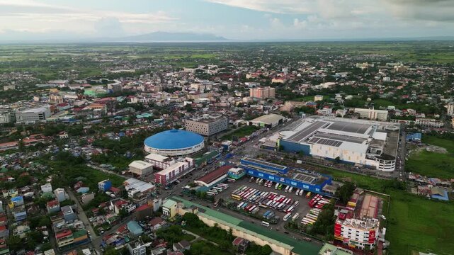Panoramic aerial orbit of bus terminal along busy roads, Jesse M Robredo Coliseum, and buildings in Naga City business district, Philippines.