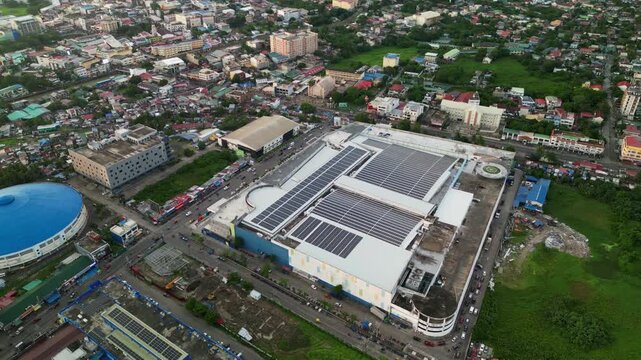 Scenic orbiting aerial view of solar panel-covered shopping mall complex amid busy streets and buildings at Naga City, Bicol, Philippines