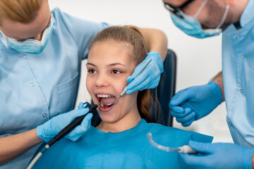 Dental checkup for young girl in clinic, featuring dentist and assistant using tools for oral care