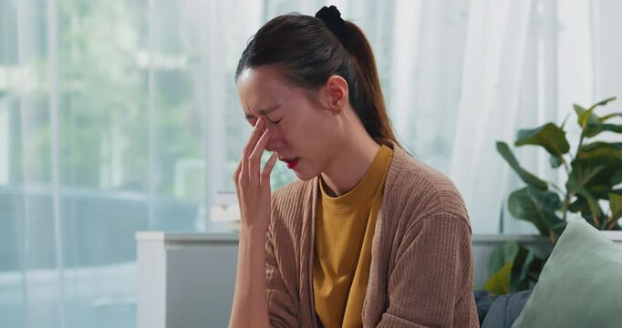 Asian woman feeling eye strain and headache while using smartphone at home, Young female suffering from dry eyes and migraine after looking at mobile phone screen for a long time.