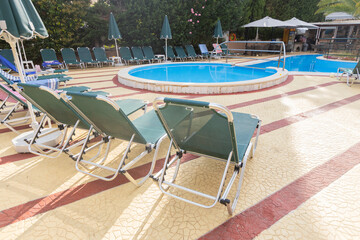 Circular resort pool with green lounge chairs and umbrellas on tiled deck in sunny setting