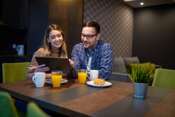 Couple enjoying breakfast together while using a tablet in a cozy cafe setting