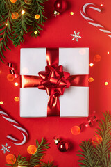 Christmas gift with red glitter decorations and Christmas tree branches on red background with bokeh. Merry Christmas and Happy New Year greeting card. Xmas and Winter holidays, top view