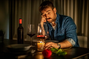 Man reflecting on love with wine and a rose during a quiet evening at home