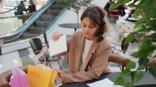 individual managing receipts and purchases, person arranging goods and taking notes calmly, customer carefully sorting and recording transactions amid contemporary shopping center environment