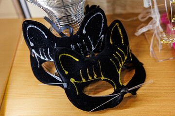 Two black masquerade masks shaped like cat faces with glittery gold and silver accents and attached whiskers, displayed on a wooden surface