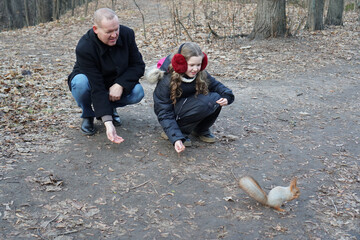 Fototapeta premium Father and daughter feeding a squirrel in a park during autumn