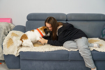 Teenage girl affectionately hugging her small Jack Russell terrier dog on a blue couch at home.