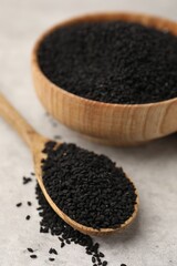 Aromatic black caraway in wooden spoon and bowl on light grey table, closeup