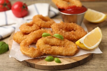 Deep fried squid rings with lemon slice, basil and ketchup on wooden table, closeup