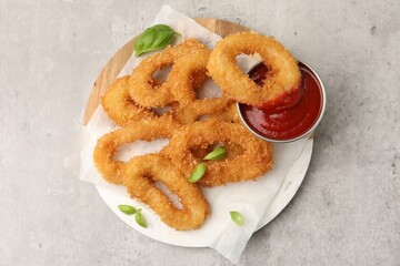Deep fried squid rings with basil and ketchup on light grey table, top view