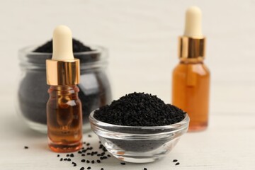 Black cumin seeds and bottles of essential oil on light wooden table, closeup