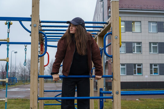 Thoughtful young woman in casual clothing standing on a playground climbing structure on an overcast day.