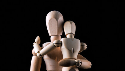 Wooden artist mannequins in close embrace under dramatic studio lighting, concept of protection and care