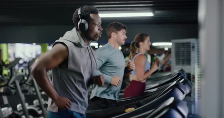 Headphones, fitness and man on treadmill in gym for running, workout or training with health. Wellness, audio tech and male person listening to music for cardio exercise on machine in sports center. - Powered by Adobe