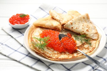 Tasty crepes with red caviar on white wooden table, closeup