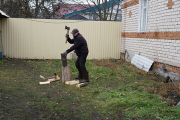 Elderly man chopping firewood with an axe in a rural backyard during autumn.