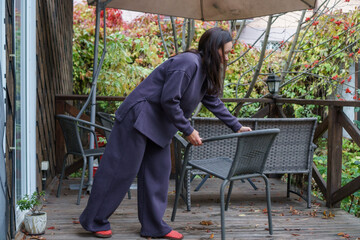 Woman in casual clothing arranging outdoor furniture on a wooden deck in autumn.