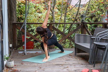 Fit woman in black activewear does yoga side angle pose on a patio in fall.