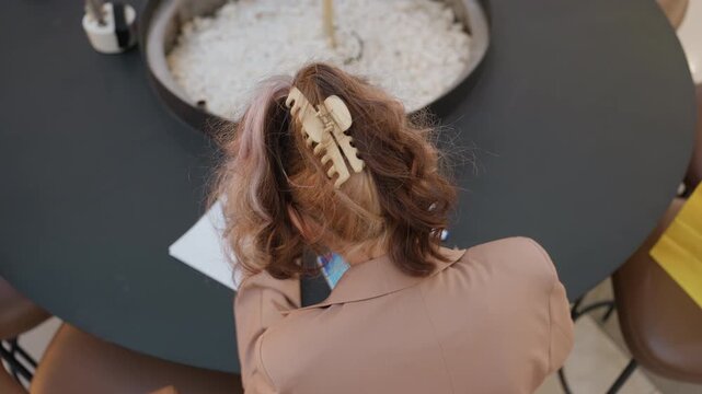 indoor restaurant woman working creatively, female figure working on project at cafe table in tranquil setting, lady drafting and sketching setup while seated at cozy cafe with decorative plants