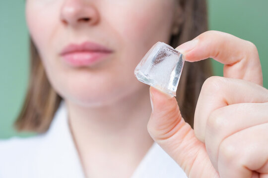 Young woman holding ice cube near her face on green background.
