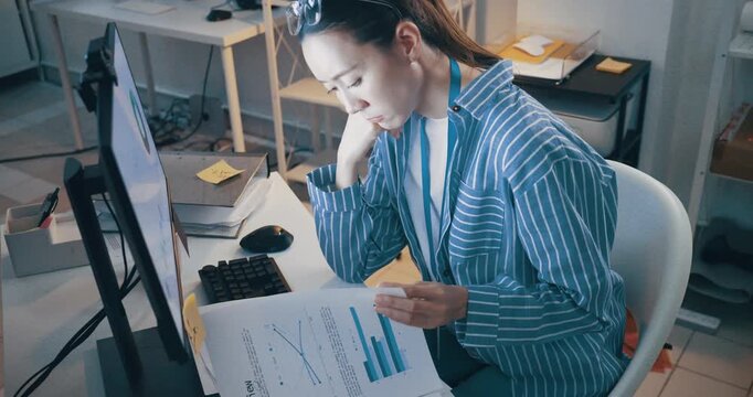 Tired female employee analyzing financial charts and feeling exhausted during a night shift.
