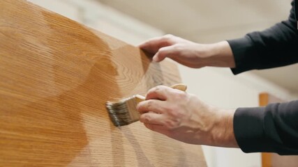 Skilled artisan applying varnish to wooden surface, showcasing craftsmanship and attention to detail, camera follows the brush movement across the grain
