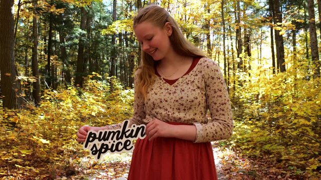 Young Woman in Golden Forest Holds Up words Pumpkin Spice in the Fall with Yellow Leaves 4K Video Stock Footage